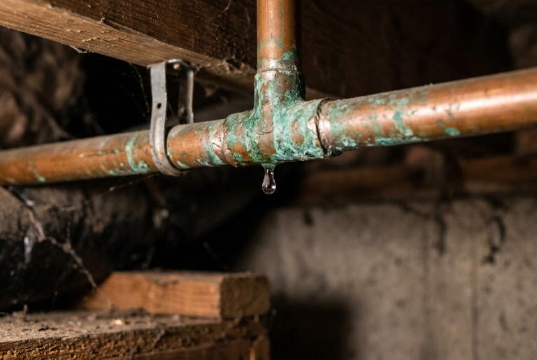 Corroded copper pipe with water drip at joint — leaky pipe signs