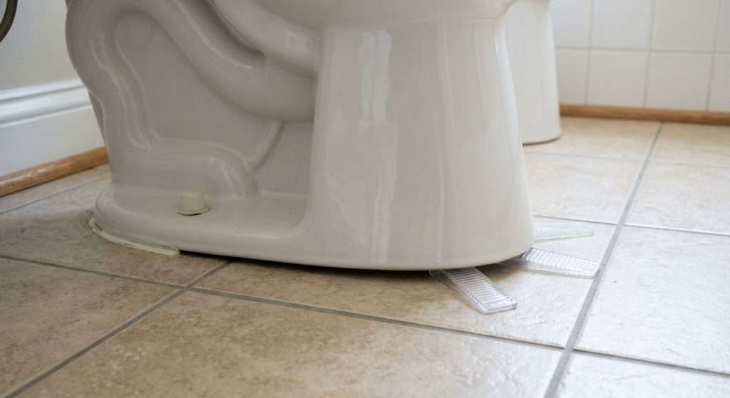 Wobbly toilet base on tile floor with plastic shims