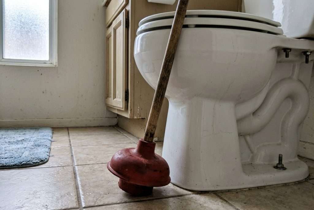 Red rubber plunger against a white toilet bowl in a home bathroom