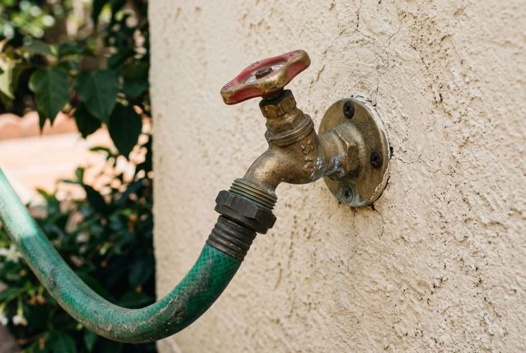 Brass hose bib outdoor faucet mounted on stucco wall with garden hose